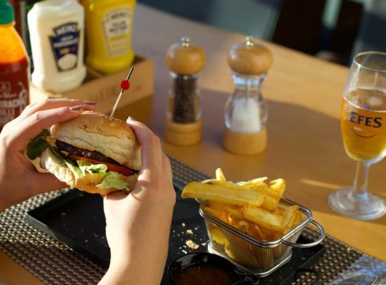 A person enjoying a delicious burger and fries with a glass of beer at a restaurant.