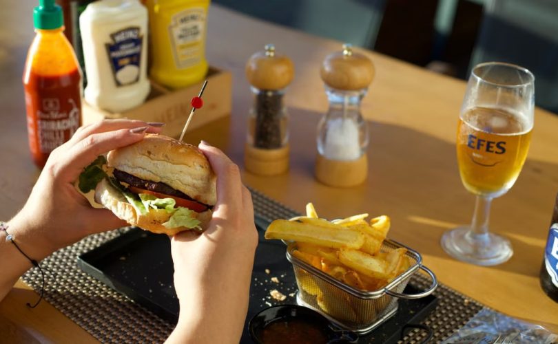 A person enjoying a delicious burger and fries with a glass of beer at a restaurant.