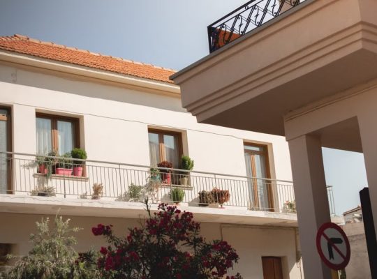 Traditional Greek house facade with potted plants and balcony details.